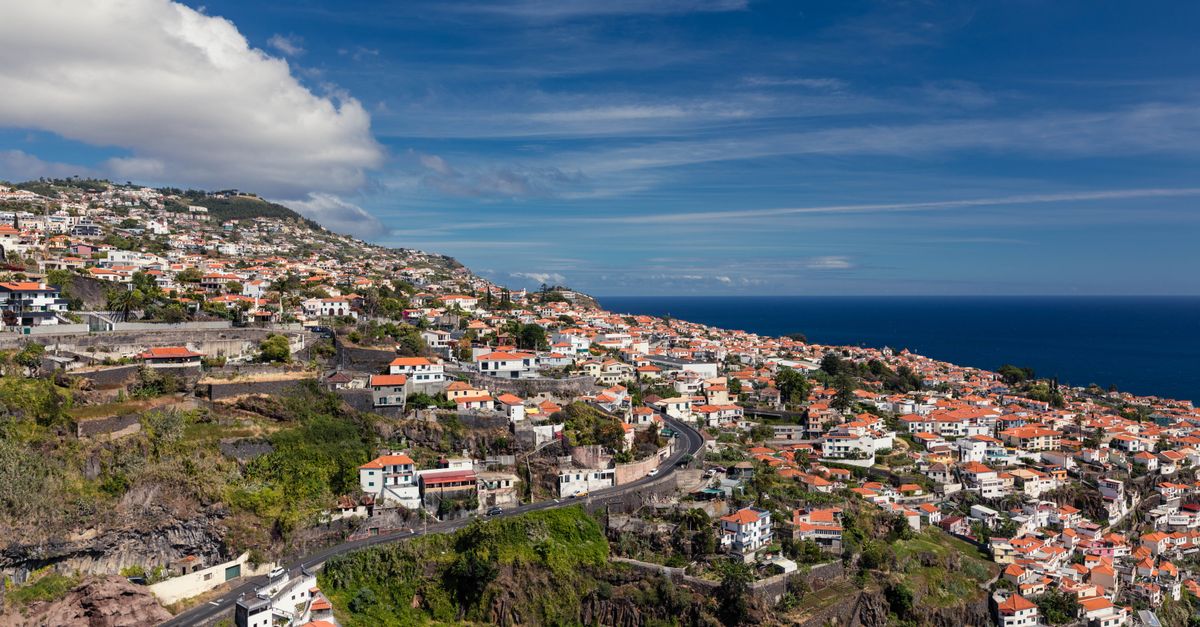View from above over Funchal: red tiled roofs on the hillside, the Atlantic behind, under a blue sky