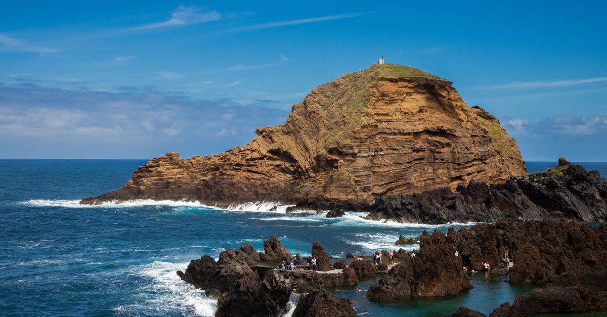 A small lighthouse on a rock off Porto Moniz's rugged coastline, Atlantic waves breaking over black volcanic rock